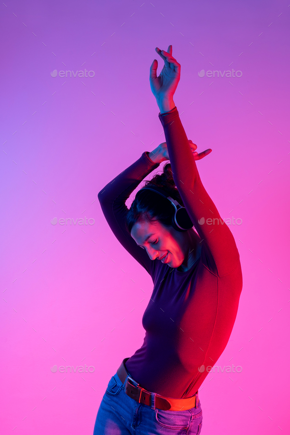 Attractive woman with headphones listening music and dancing in studio with blue and red lights